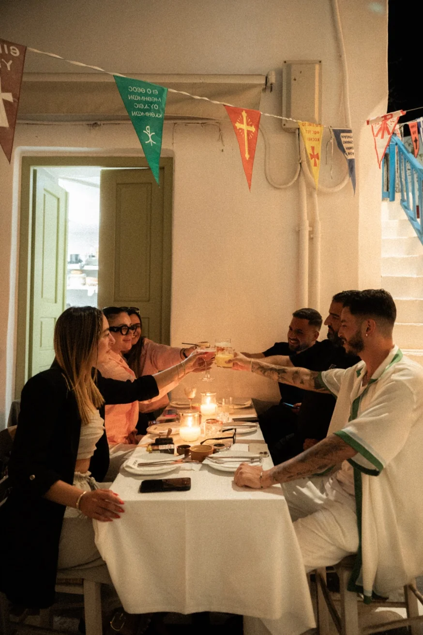 Group of guests toasting cocktails at a candlelit dinner at Pūblico, Mykonos Town