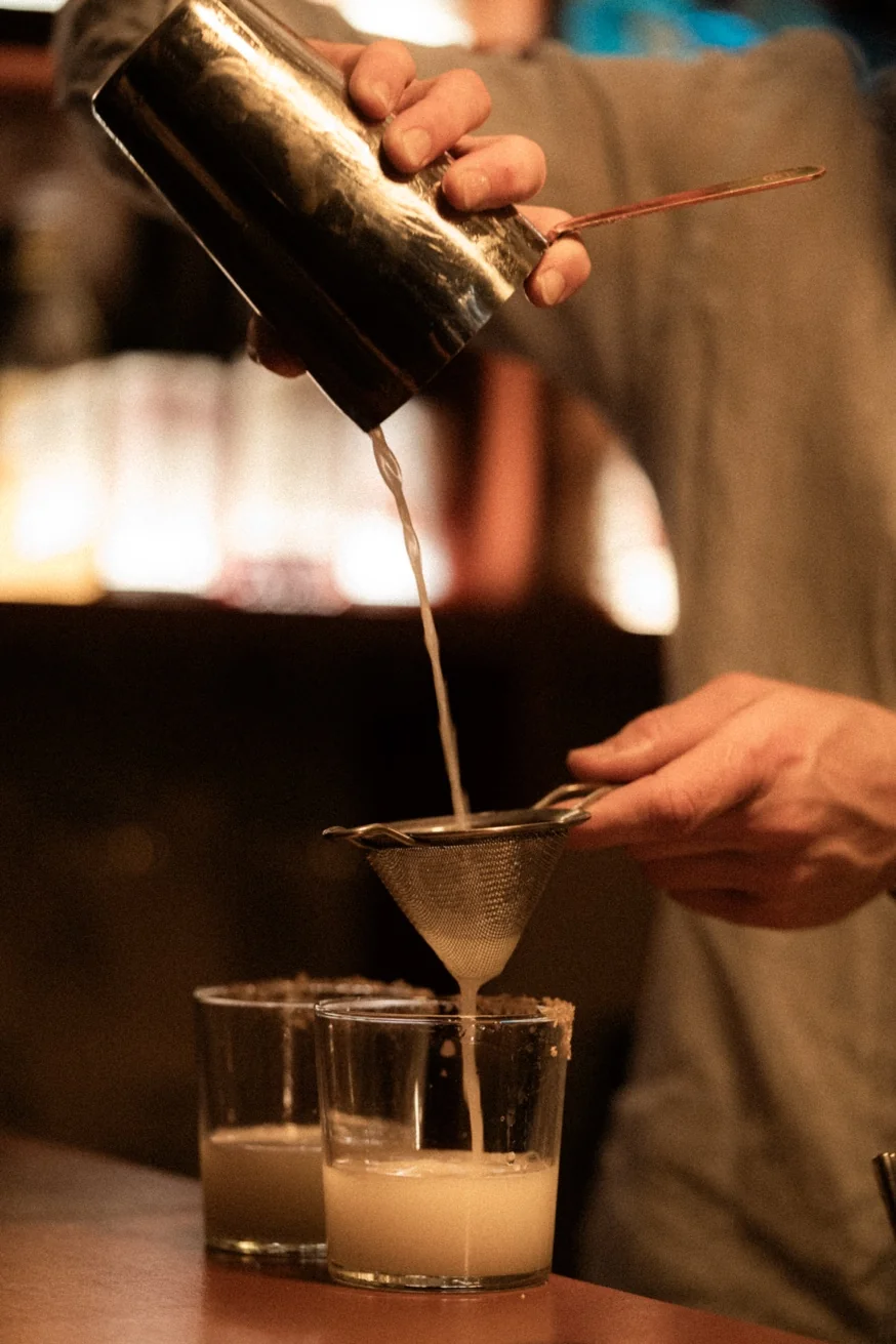 Bartender straining a fresh mezcal margarita through a fine sieve at Pūblico Mezcaleria — handcrafted cocktails in Mykonos Town