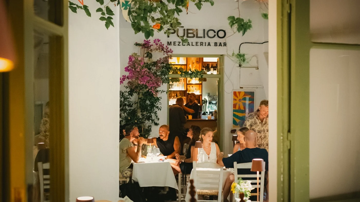 Pūblico Restaurant & Mezcaleria Bar in Mykonos Town — outdoor terrace dining with bougainvillea, guests and glowing bar in the heart of Mykonos Old Town